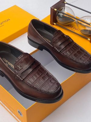 Men's chocolate brown Louis Vuitton crocodile-embossed penny loafers with metal LV hardware and rubber-injected heel, displayed with branded orange shoebox and hourglass on white surface.