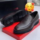 Roberto Cavalli men’s brown textured leather loafers with embossed RC monogram and rugged lug sole, displayed beside branded black box, poodle figurine, and stacked books on light wood surface.