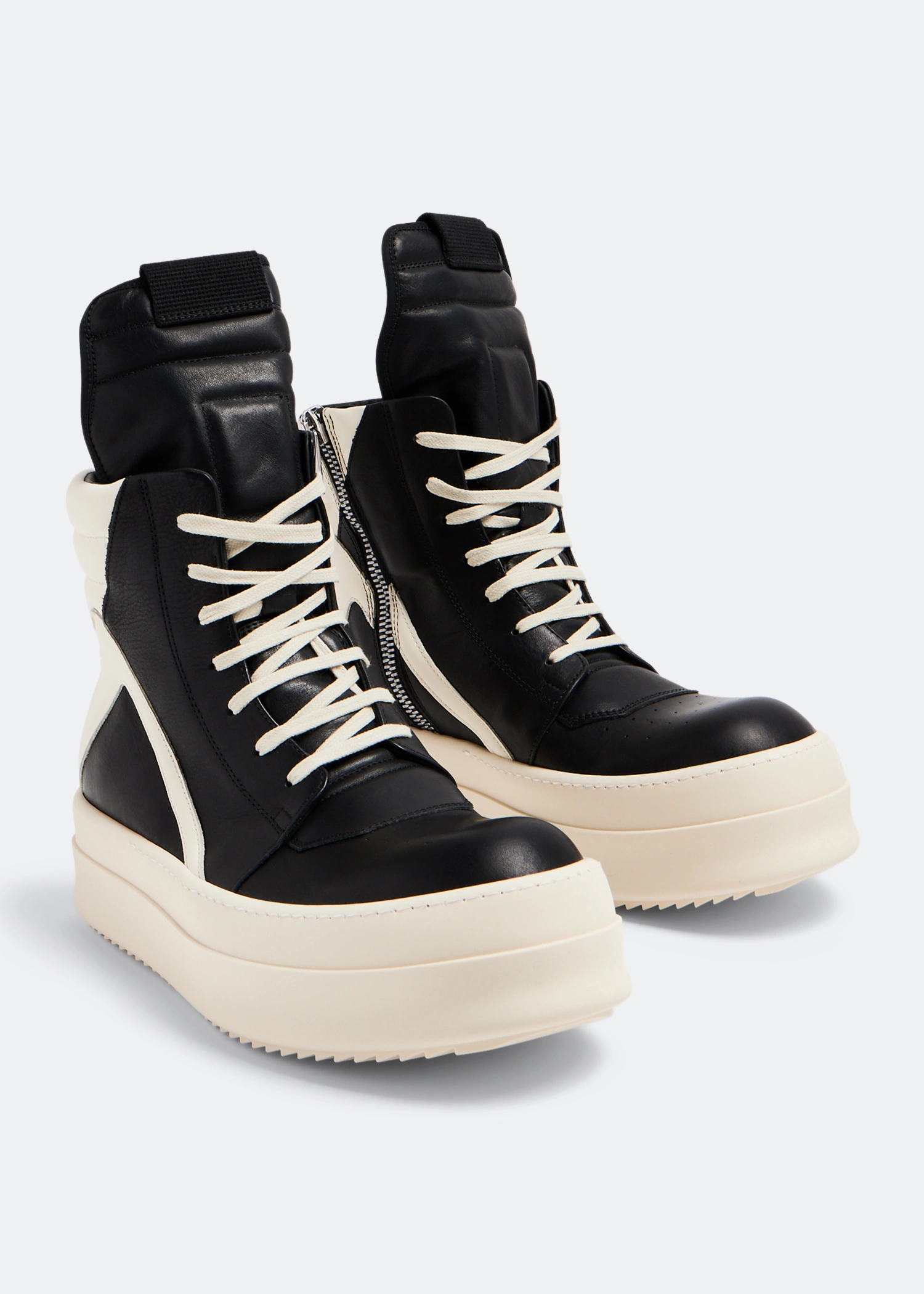 Black and cream high-top platform sneakers Men's black and cream high-top platform sneakers with thick white sole and side zipper, displayed on blue shoebox with fashion books and KAWS figurine in background.