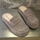 FDCP men's taupe suede penny loafer mules with braided strap detail and thick rubber sole, displayed on metallic surface against stone wall background.