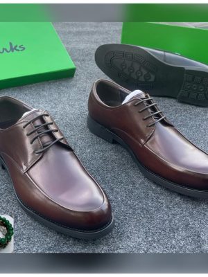 Clarks men’s brown leather plain-toe derby dress shoes with polished finish and cushioned sole, displayed beside green branded box on grey carpet background.