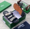 miSter men’s black and snakeskin triple-strap slides with gold “M” hardware and tan-accented sole, displayed beside green branded box and hourglass on textured surface.