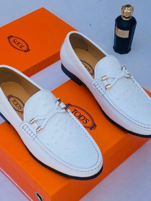 Tod’s men’s brown ostrich-embossed leather loafers with gold hardware and Gommino sole, displayed beside orange branded box and perfume bottle on white surface.