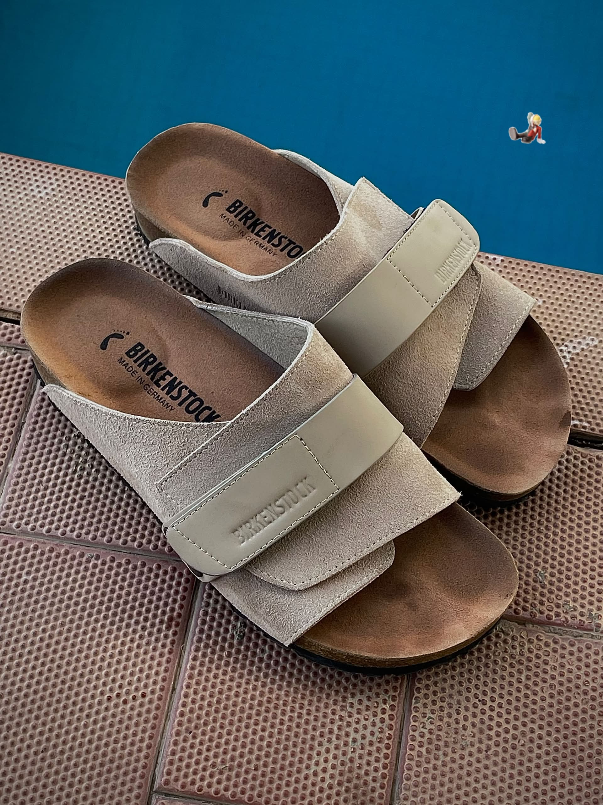 Authentic Birkenstock Arizona sandals Birkenstock Arizona men's sandals in black suede with adjustable buckle straps and cork-latex footbed, displayed next to original blue Birkenstock shoebox on grey wood surface.