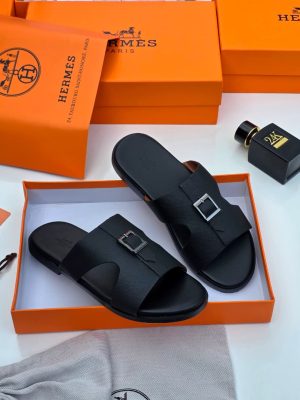 Hermès men’s black Epsom leather Oran slide sandals with signature H-cutout, displayed in orange Hermès box with branded dust bag and perfume bottle on white surface.