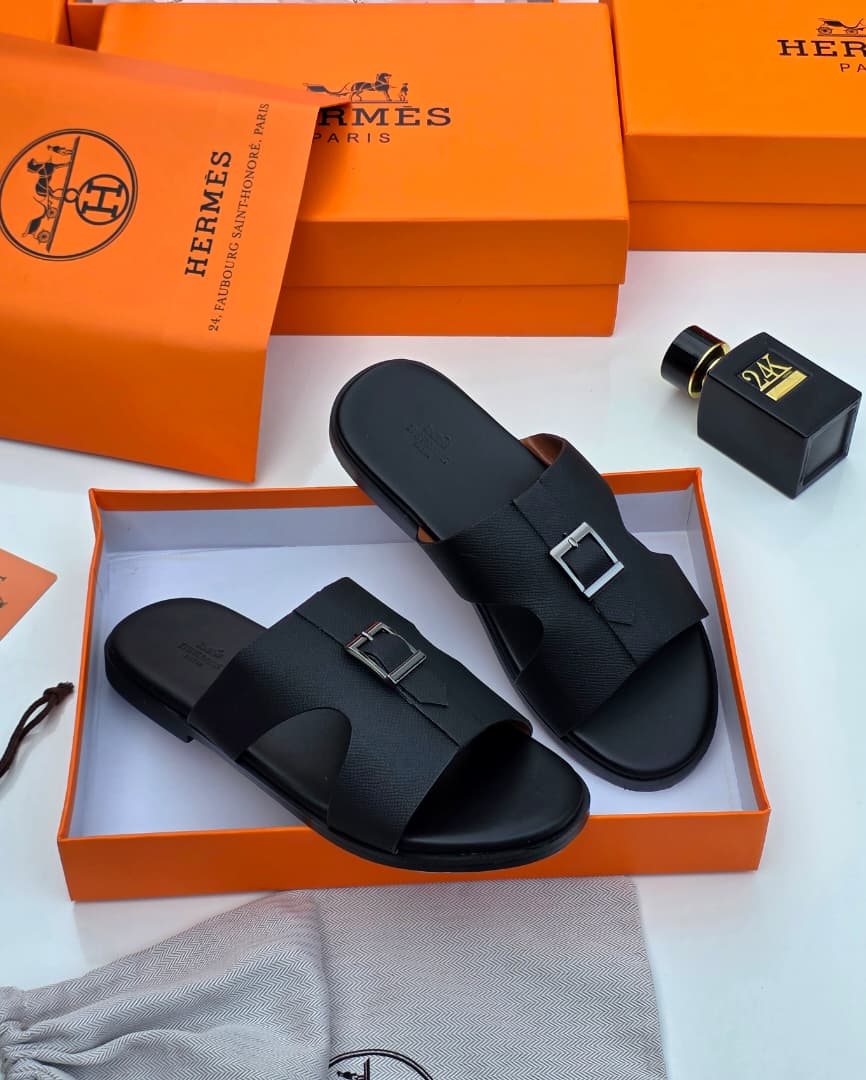 Hermès Oran sandals in black Epsom leather Hermès men’s black Epsom leather Oran slide sandals with signature H-cutout, displayed in orange Hermès box with branded dust bag and perfume bottle on white surface.
