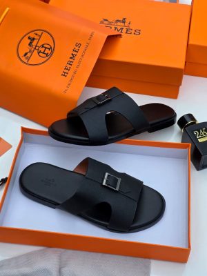Hermès men’s black Epsom leather Oran slide sandals with signature H-cutout, displayed in orange Hermès box with branded dust bag and perfume bottle on white surface.