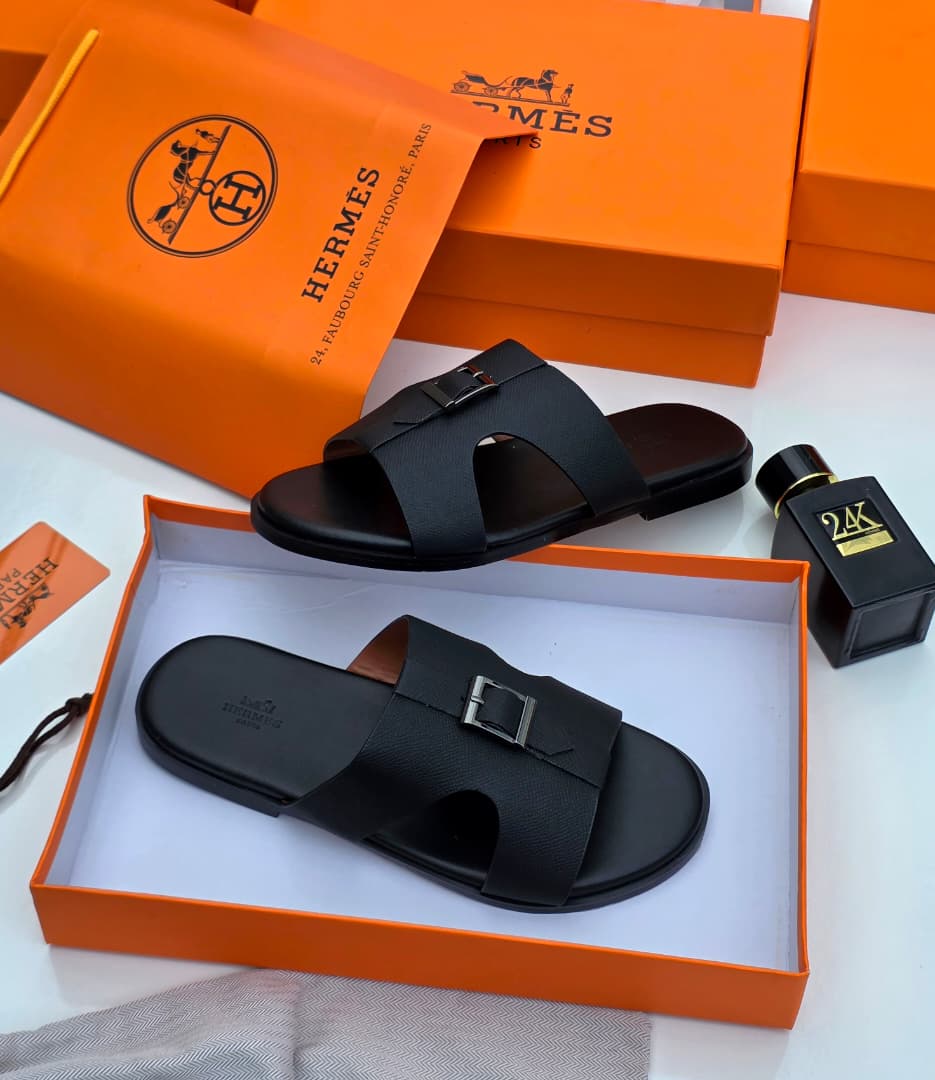 Hermès Oran sandals in black Epsom leather Hermès men’s black Epsom leather Oran slide sandals with signature H-cutout, displayed in orange Hermès box with branded dust bag and perfume bottle on white surface.