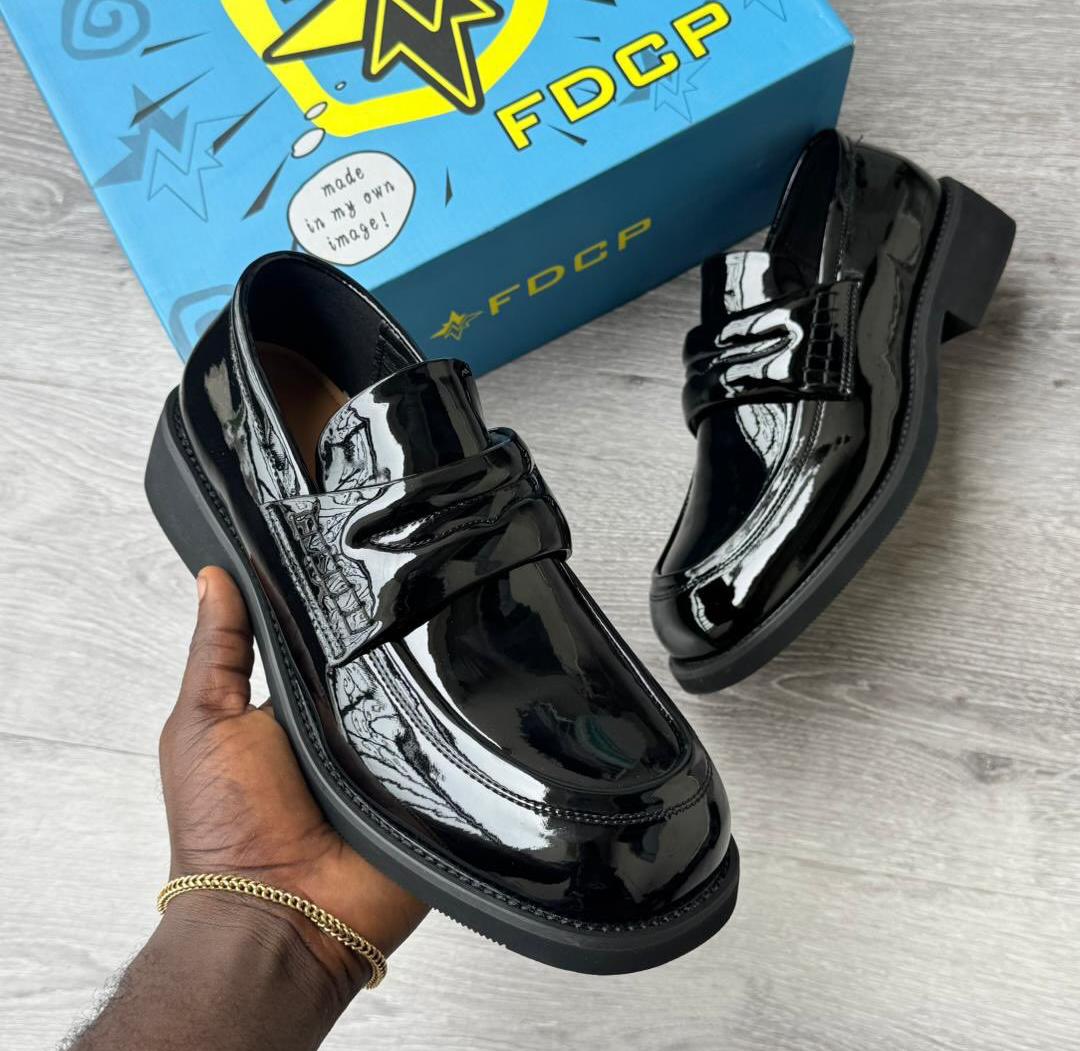 FDCP burgundy patent leather penny loafers FDCP men's burgundy high-gloss patent leather penny loafers with thick chunky black rubber sole, held in hand with branded blue FDCP shoebox in background.