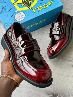 FDCP men's burgundy high-gloss patent leather penny loafers with thick chunky black rubber sole, held in hand with branded blue FDCP shoebox in background.