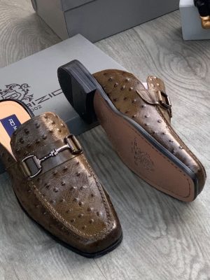 Men's brown ostrich leather horsebit mules with square toe and stacked heel, displayed on grey wood floor with branded shoebox.