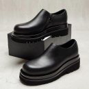 Men's black leather chunky Chelsea boots with side zipper and thick ridged platform sole, displayed on grey block against marble background.