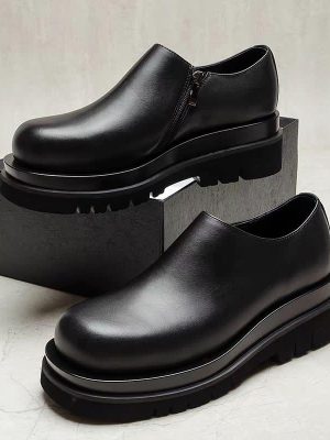 Men's black leather chunky Chelsea boots with side zipper and thick ridged platform sole, displayed on grey block against marble background.