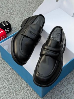 Men's chocolate brown leather penny loafers with black rubber sole, displayed in open blue shoebox with decorative dice on grey carpet.