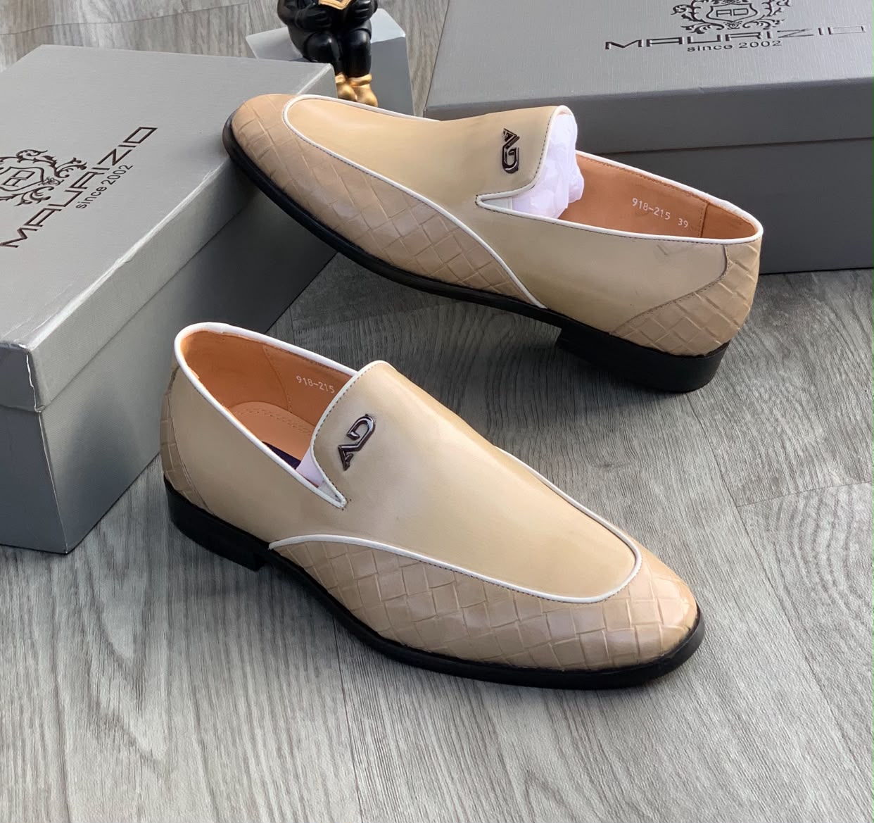 Maurizidio beige woven leather loafers Men's beige Maurizidio woven leather loafers with white piping, metallic logo, and black rubber sole, displayed on grey wood floor with branded shoebox.
