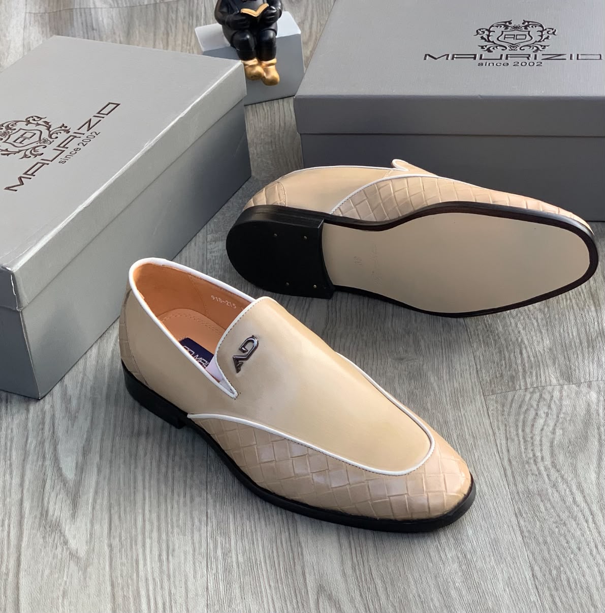 Maurizidio beige woven leather loafers Men's beige Maurizidio woven leather loafers with white piping, metallic logo, and black rubber sole, displayed on grey wood floor with branded shoebox.