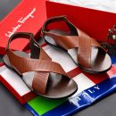 Men’s brown leather cross-strap sandals with perforated detailing and slingback heel, held by hand beside yellow and red beaded bracelet on white background.