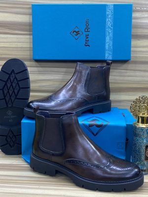 Men's brown leather Steve Riots combat boots with thick ridged platform sole, displayed on wooden surface with branded blue shoebox and decorative perfume bottle.