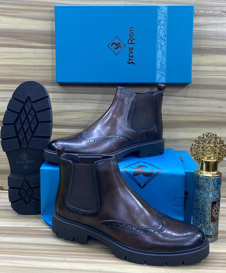 Steve Riots dark brown brogue Chelsea boots Men's brown leather Steve Riots combat boots with thick ridged platform sole, displayed on wooden surface with branded blue shoebox and decorative perfume bottle.