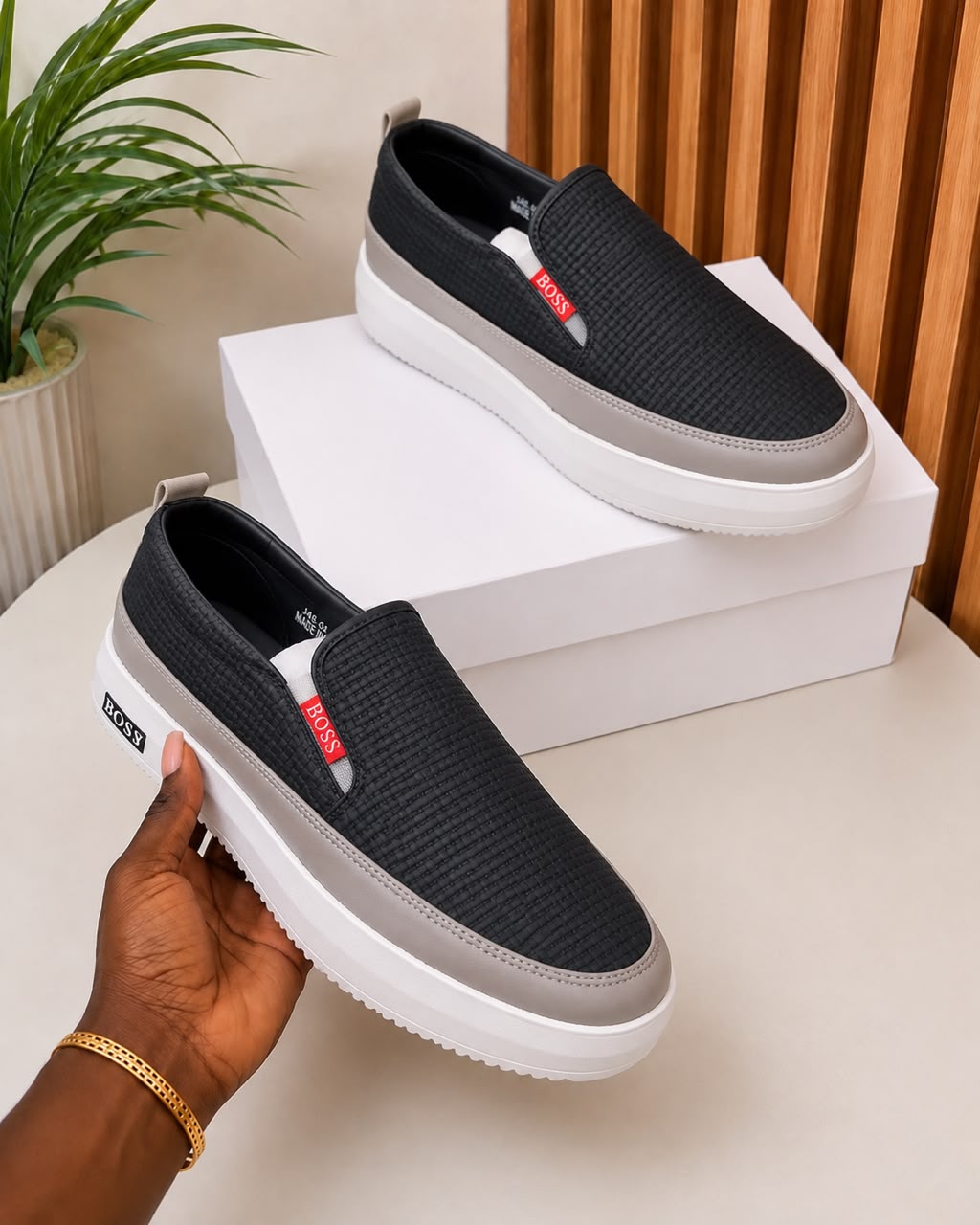 Hugo Boss woven slip-on sneakers Hugo Boss men's beige woven slip-on sneakers with brown leather trim, red logo tag, and white platform sole, held in hand with white shoebox on beige surface.