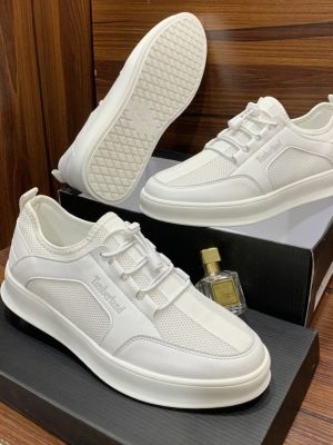 Timberland men's all-white leather and mesh lace-up sneakers with thick white rubber sole, displayed on black shoeboxes with a perfume bottle.