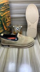 Timberland men's beige suede slip-on sneakers with perforated upper, navy elastic panels, and cream rubber sole, displayed on wooden floor with branded packaging.