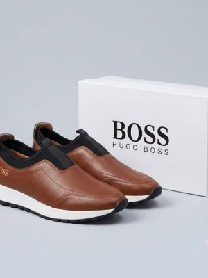 Hugo Boss men's brown pebbled leather slip-on sneakers with black elastic panels and white midsole, displayed with branded white shoebox on a grey surface.