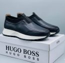 Hugo Boss men's brown pebbled leather slip-on sneakers with black elastic panels and white midsole, displayed with branded white shoebox on a grey surface.