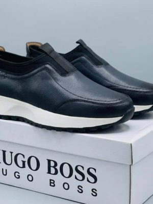 Hugo Boss men's brown pebbled leather slip-on sneakers with black elastic panels and white midsole, displayed with branded white shoebox on a grey surface.