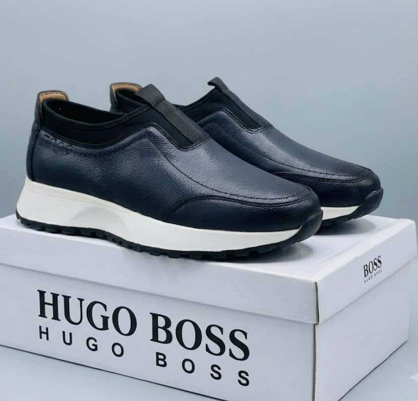 Hugo Boss pebbled leather slip-on sneakers Hugo Boss men's brown pebbled leather slip-on sneakers with black elastic panels and white midsole, displayed with branded white shoebox on a grey surface.