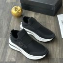 Emporio Armani men's black and red slip-on sneakers with metallic eagle logo and thick white rubber sole, displayed on a grey wood floor with a black branded shoebox and gold apple decor.