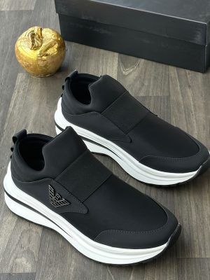 Emporio Armani men's black and red slip-on sneakers with metallic eagle logo and thick white rubber sole, displayed on a grey wood floor with a black branded shoebox and gold apple decor.